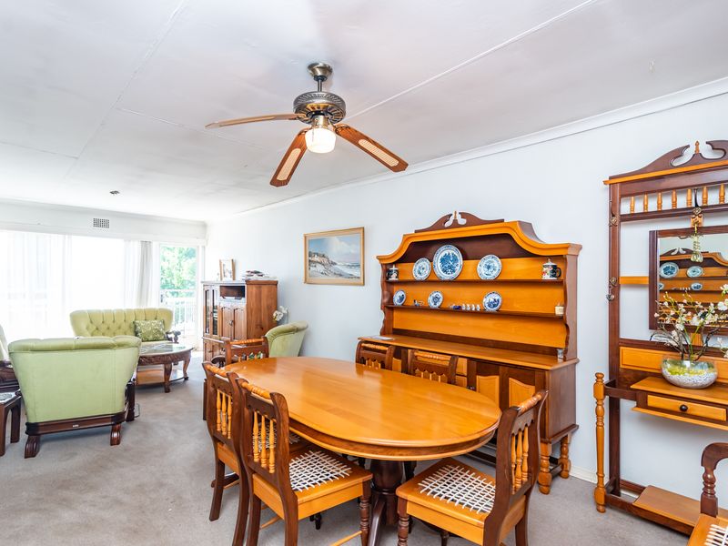 Open-plan living and dining area featuring a ceiling fan, carpeted flooring, and access to an outdoor balcony through sliding glass doors.