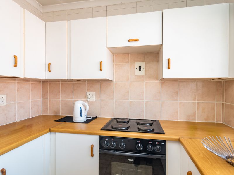 A functional kitchen featuring white cabinetry, wood-look laminate countertops, and a tiled backsplash with a built-in electric oven and hob.