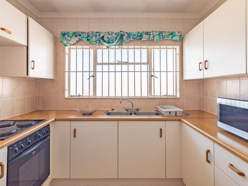 A functional kitchen featuring white cabinetry, laminate countertops, a double stainless steel sink, and a built-in electric oven and hob.