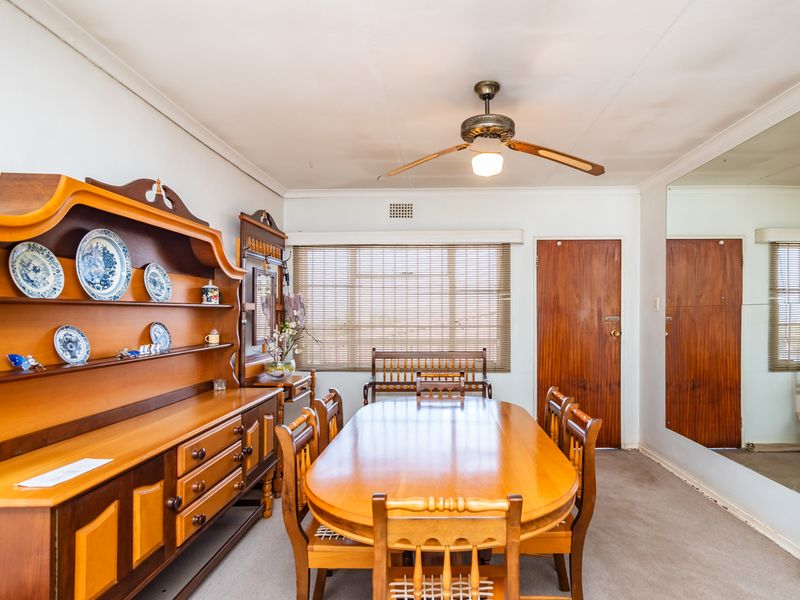 A dining room featuring a ceiling fan, venetian blinds, and a large wall-mounted mirror, with carpet flooring throughout.