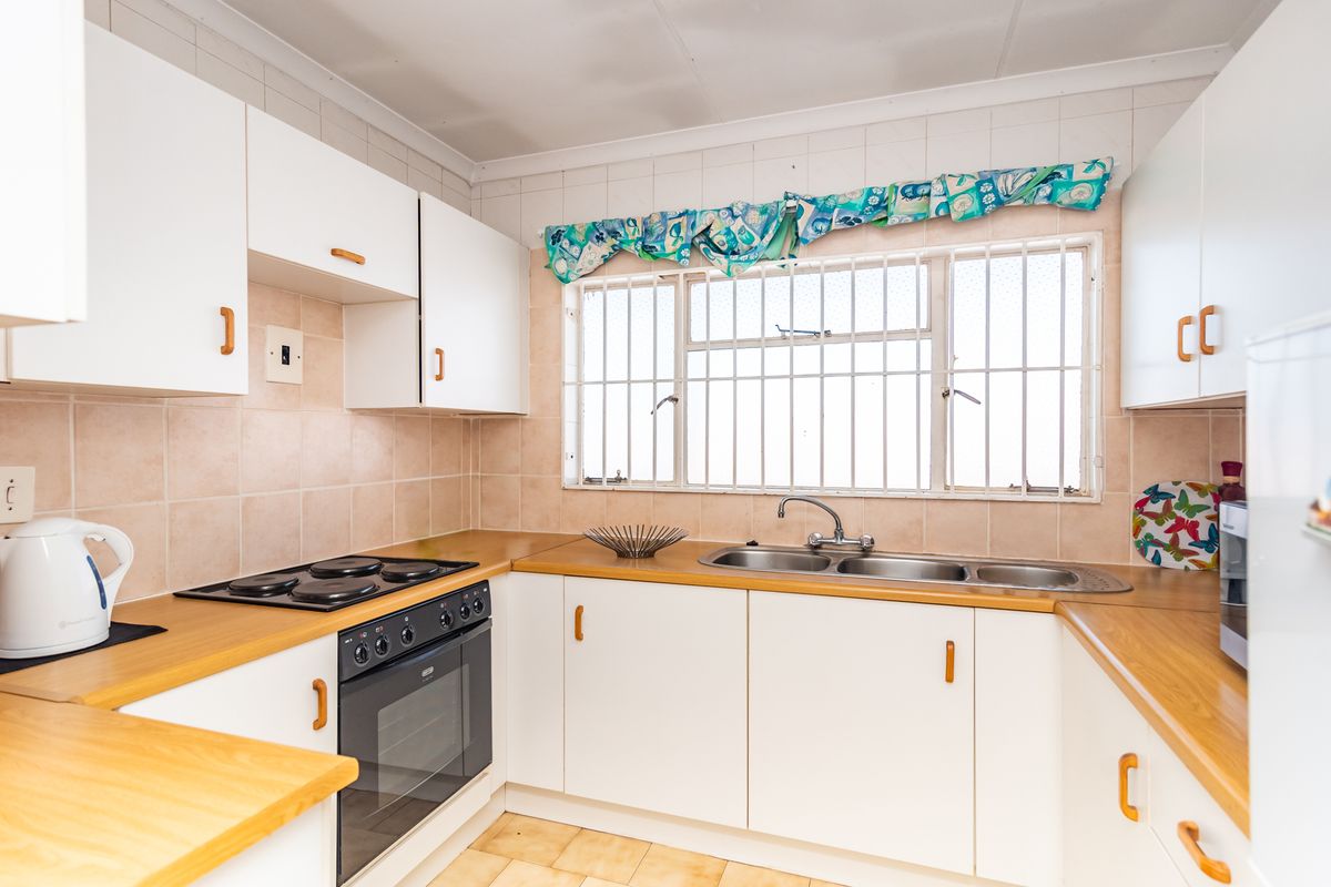 A functional kitchen featuring white cabinetry, laminate countertops, an electric hob, built-in oven, and a double stainless steel sink with tiled backsplash.