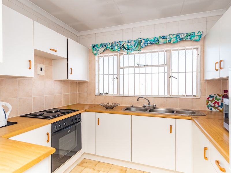 A functional kitchen featuring white cabinetry, laminate countertops, an electric hob, built-in oven, and a double stainless steel sink with tiled backsplash.
