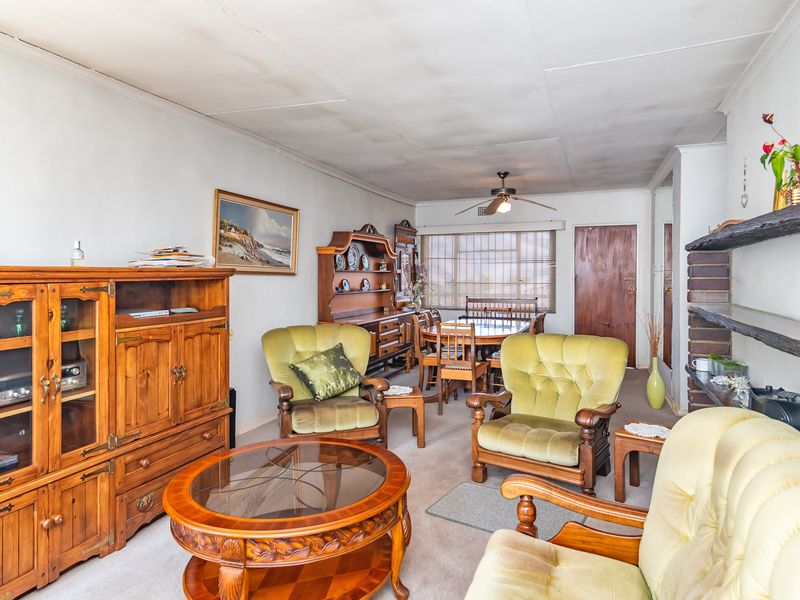 Open plan living and dining area featuring a brick accent wall, ceiling fan, and neutral carpeting, offering a functional layout with potential for modernization.