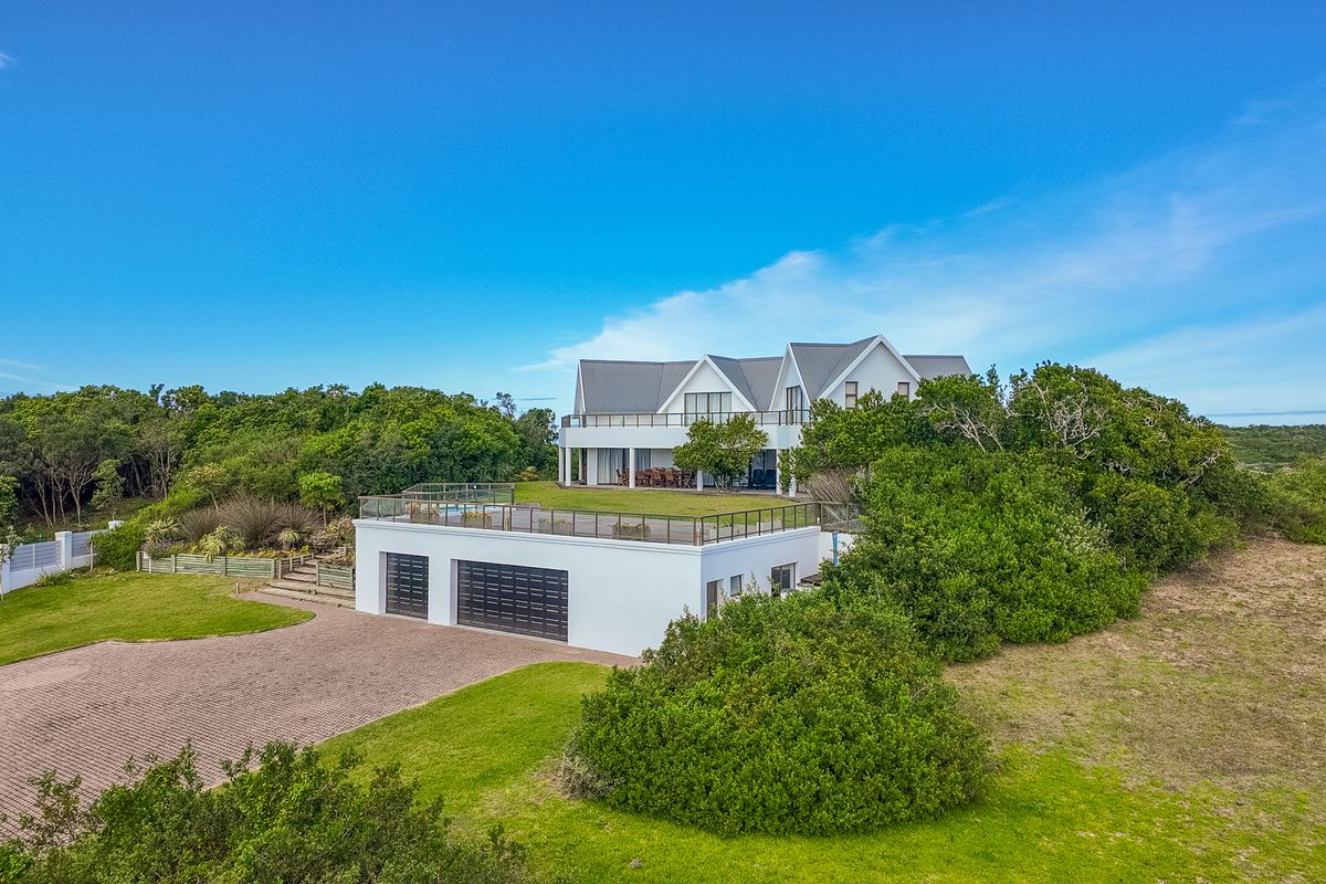 Aerial view of a modern multi-level residence featuring a paved driveway, double garage, and an expansive rooftop deck with glass balustrades.