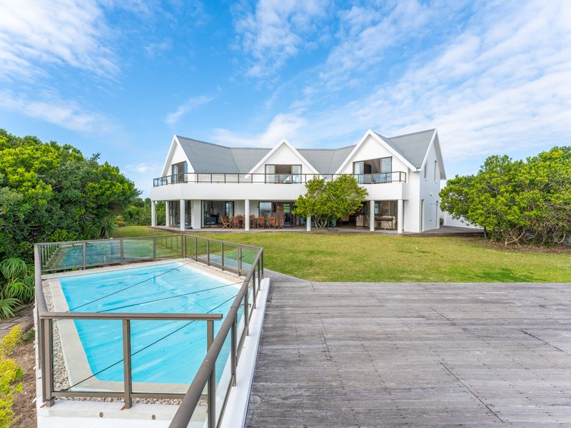 Rear view of a modern house featuring a swimming pool with glass fencing, expansive timber decking, a covered patio, and a spacious upper-level balcony.