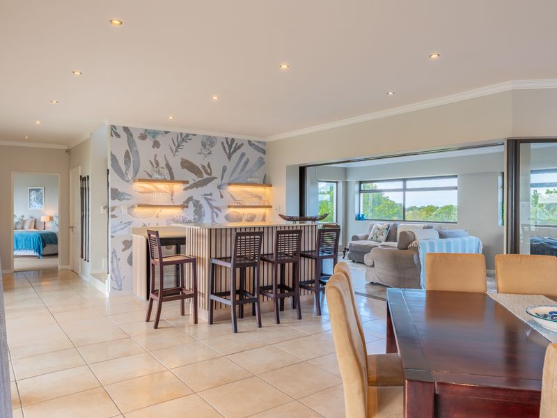 Spacious open-plan living area featuring a built-in bar, tiled flooring, and large sliding doors leading to an outdoor space with scenic views.