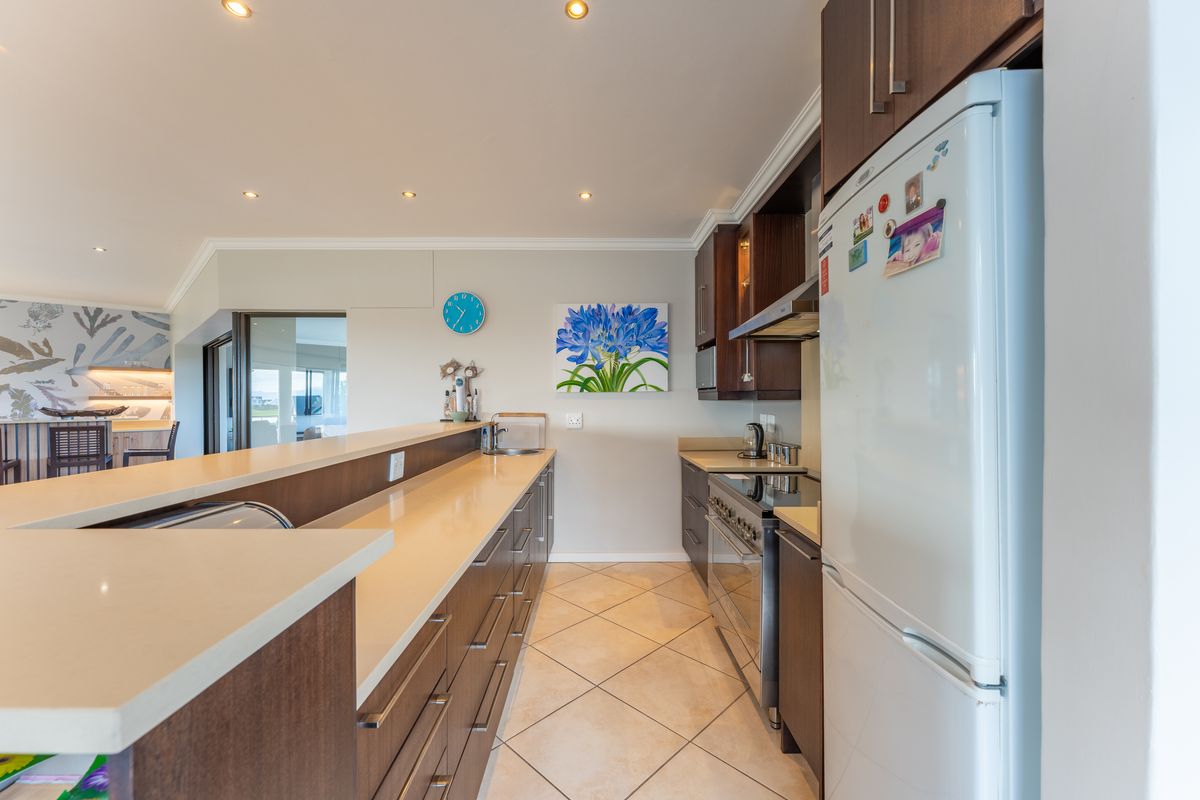 Modern kitchen featuring dark wood cabinetry, stone countertops, stainless steel gas stove, and tiled flooring, seamlessly integrated into an open-plan living space.