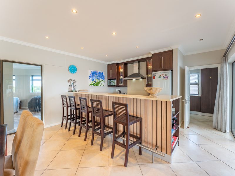 Open plan kitchen area featuring a breakfast bar, dark wood cabinetry, stainless steel extractor fan, and tiled flooring with access to outdoor space.