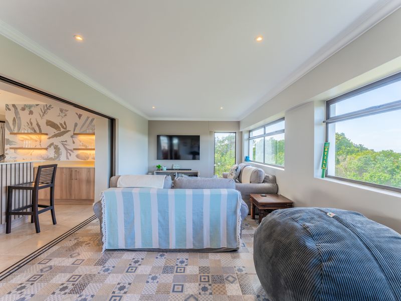Spacious open-plan living area featuring large windows, recessed lighting, and a seamless transition to an adjacent bar area with built-in cabinetry.