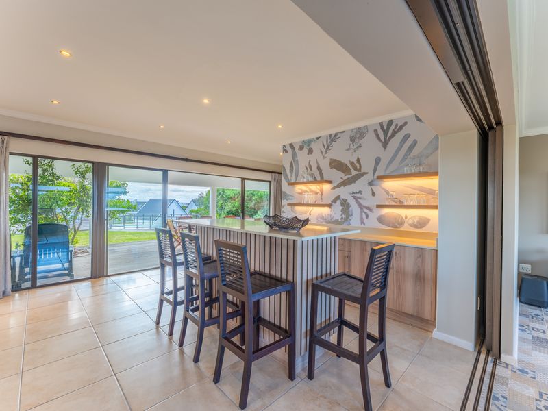 A modern, well-lit indoor bar area featuring a built-in counter, custom cabinetry with floating shelves, and large sliding glass doors opening to the patio.