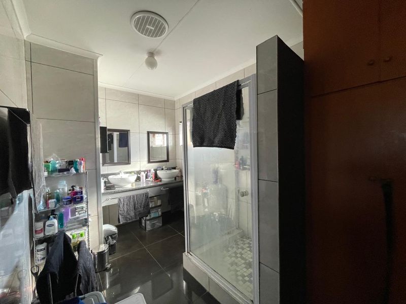 A functional bathroom featuring a double vanity with vessel sinks, a glass-enclosed shower, and neutral wall and floor tiling.