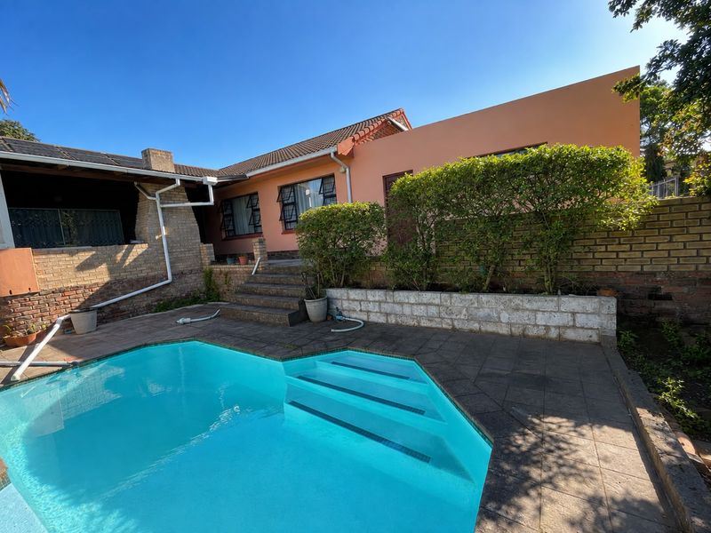 Outdoor pool area featuring a paved patio, brick retaining wall, and stone steps leading to the rear elevation of the house.