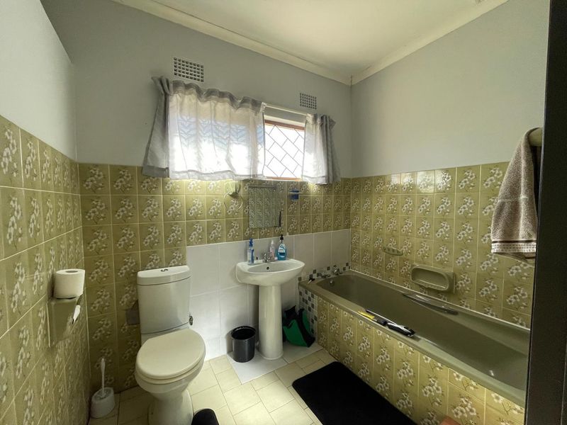 A dated bathroom featuring a pedestal sink, toilet, and bathtub with original patterned ceramic wall tiles.