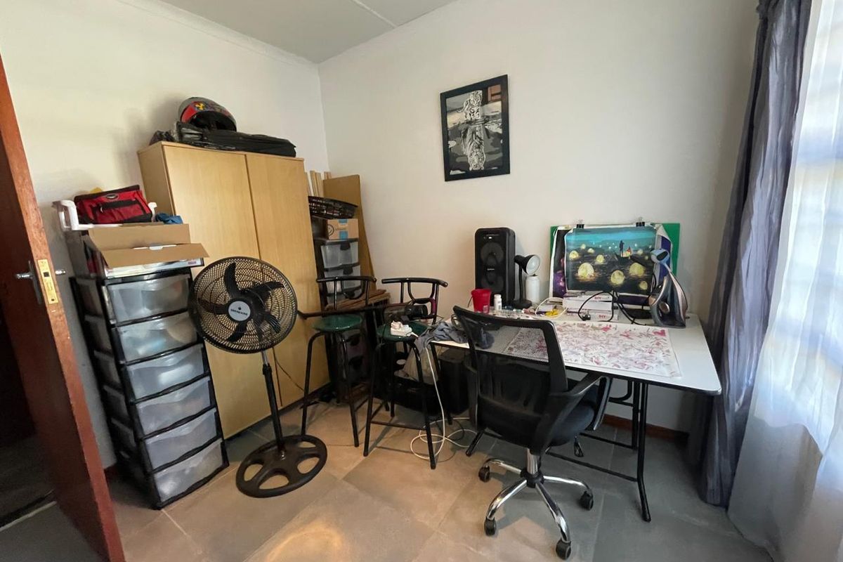 A functional bedroom space featuring tiled flooring and neutral wall finishes, currently utilized as a home office area.