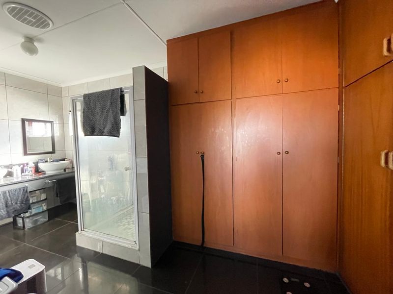 Bathroom featuring a shower enclosure, vanity basin, and extensive built-in wooden cabinetry with dark tiled flooring and wall finishes.