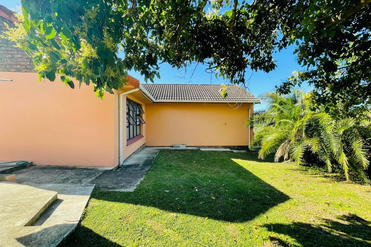 Rear view of the house featuring a lawn area, concrete pathway, and tiled roof structure.