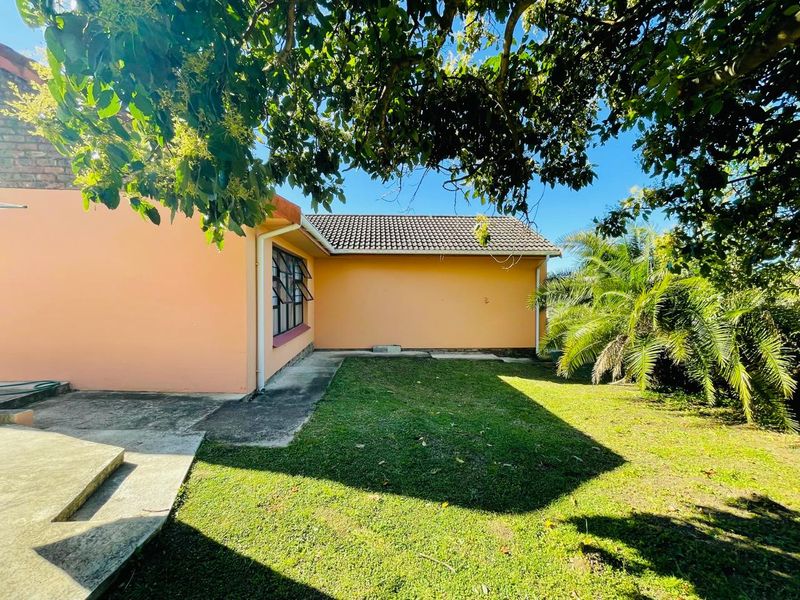 Rear view of the house featuring a lawn area, concrete pathway, and tiled roof structure.
