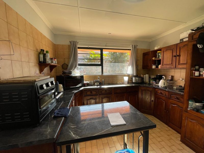 A functional kitchen featuring traditional wooden cabinetry, dark laminate countertops, and tiled backsplash, offering a classic layout with potential for modern updates.