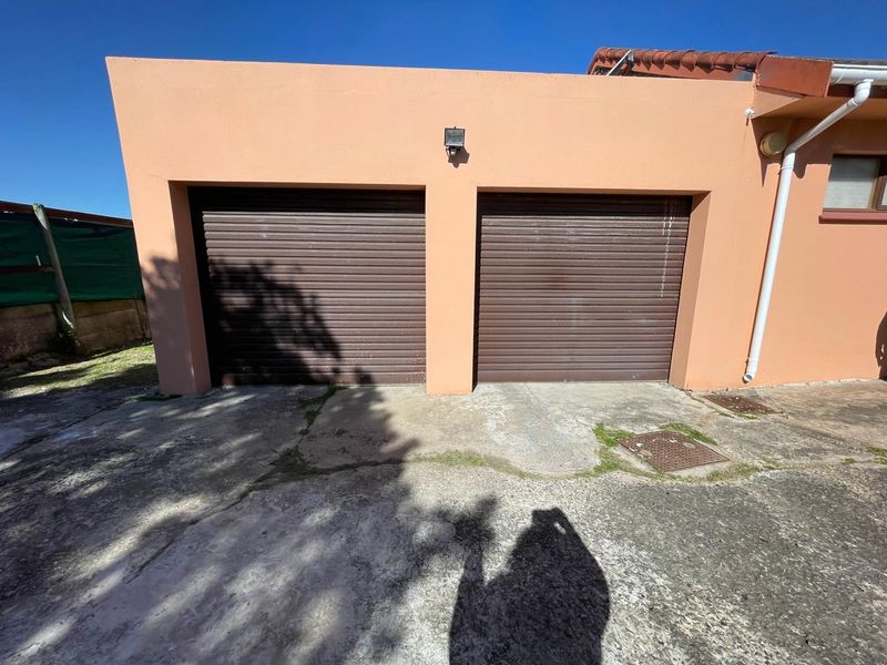 A double garage exterior featuring two brown roller doors and a concrete driveway with visible surface cracking and weathering.