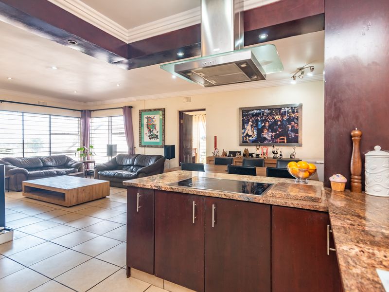 Spacious open-plan living and kitchen area featuring granite countertops, dark wood cabinetry, a central cooktop with extractor fan, and tiled flooring throughout.