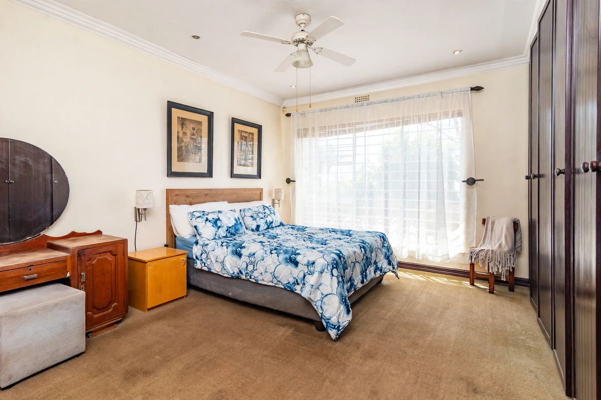 A well-proportioned bedroom featuring built-in cupboards, carpeted flooring, a ceiling fan, and large windows allowing for natural light.