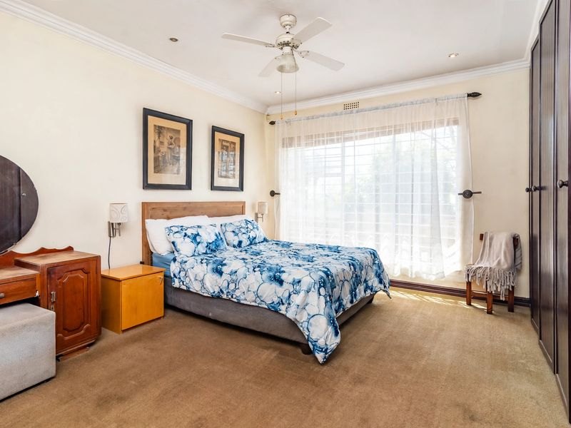 A well-proportioned bedroom featuring built-in cupboards, carpeted flooring, a ceiling fan, and large windows allowing for natural light.