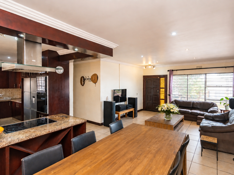 Spacious open-plan living area featuring a kitchen with granite countertops, built-in appliances, and tiled flooring throughout, seamlessly connecting to the dining and lounge space.