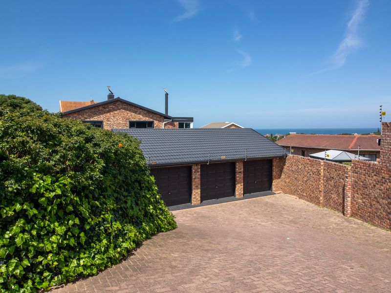 A well-maintained triple garage with a paved driveway, brick boundary walls, and electric fencing, set against a clear blue sky.