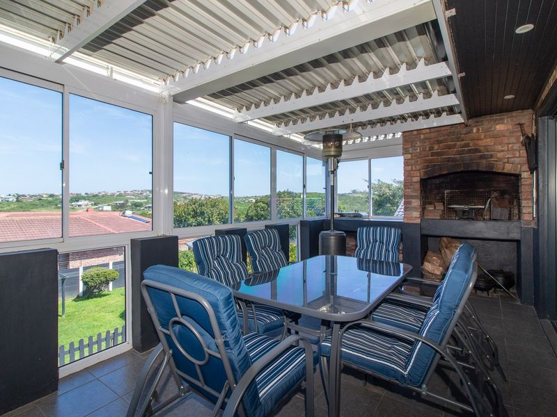 Enclosed patio area featuring a built-in brick braai, tiled flooring, and large sliding windows offering scenic views.