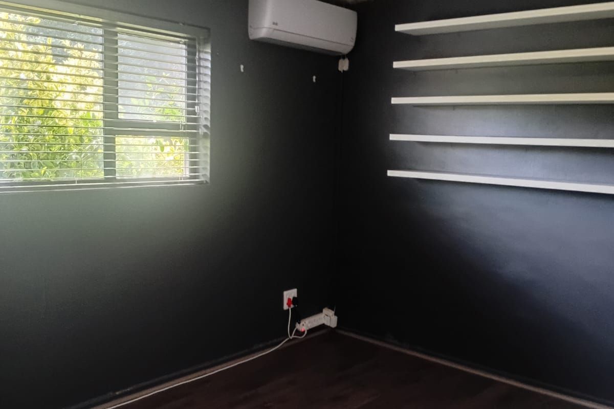 A bedroom featuring dark walls, laminate flooring, floating shelves, and a split-system air conditioner.