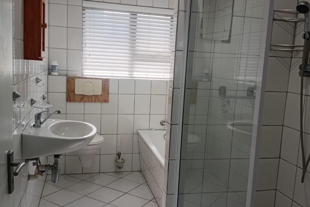 A functional bathroom featuring a shower enclosure, built-in bathtub, and wall-mounted basin with tiled finishes throughout.