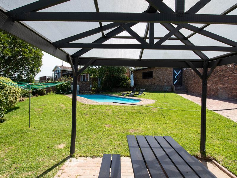 Outdoor entertainment area featuring a swimming pool, lawn, and a covered gazebo structure set against a brick-walled garden.