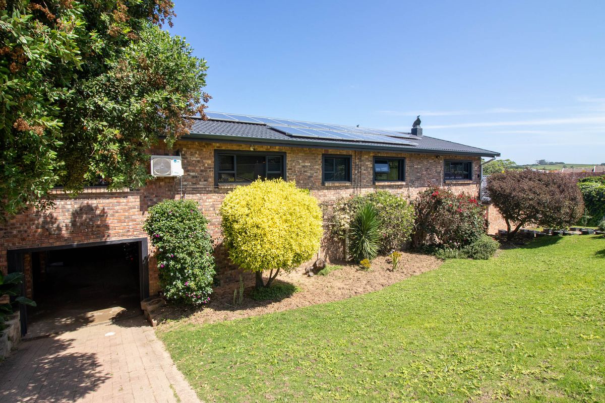 Rear view of a brick house featuring a lawn, paved driveway, integrated garage, and roof-mounted solar panels.