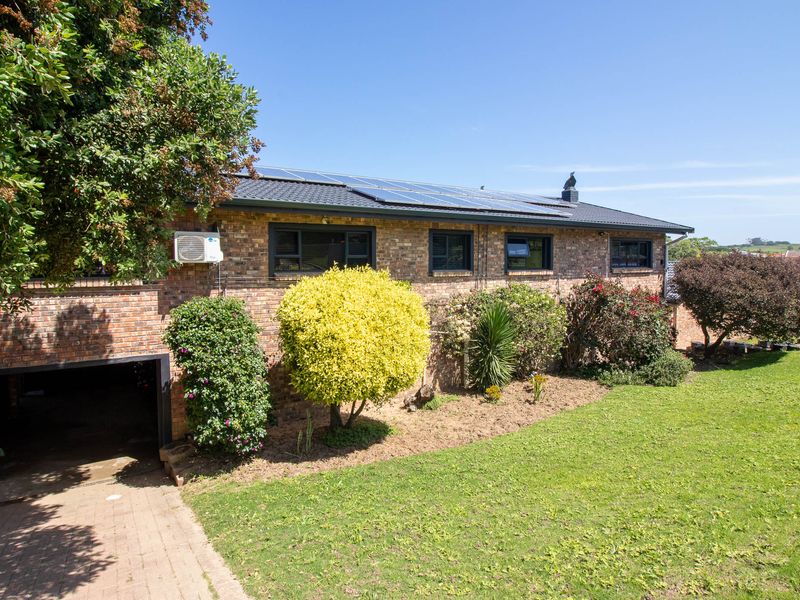 Rear view of a brick house featuring a lawn, paved driveway, integrated garage, and roof-mounted solar panels.