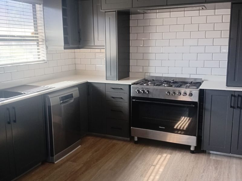 Modern kitchen featuring dark cabinetry, white subway tile backsplash, stainless steel gas stove, and integrated dishwasher with light wood-look flooring.