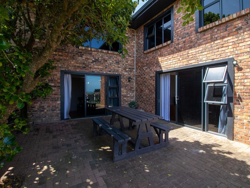 A paved outdoor patio area featuring exposed brick walls and large sliding glass doors providing access to the interior living spaces.