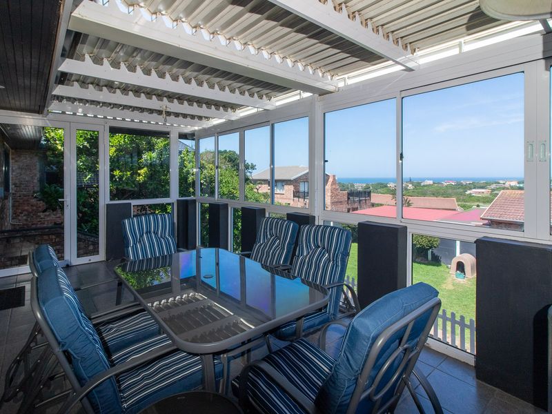 Enclosed patio area featuring tiled flooring, corrugated roofing, and large sliding glass windows offering scenic coastal views.
