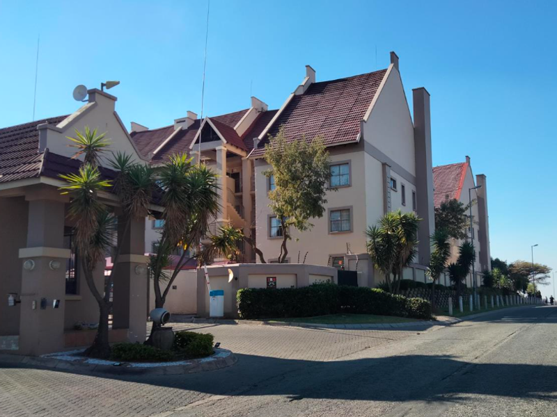 Front elevation of a multi-story apartment complex featuring a paved entrance, security gate, and well-maintained exterior facade with tiled roofing.