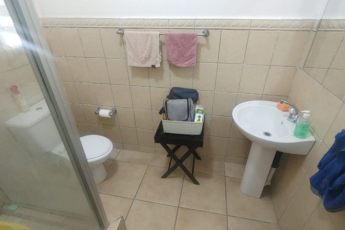 A functional bathroom featuring a pedestal washbasin, toilet, and a glass-enclosed shower with neutral ceramic wall and floor tiling.