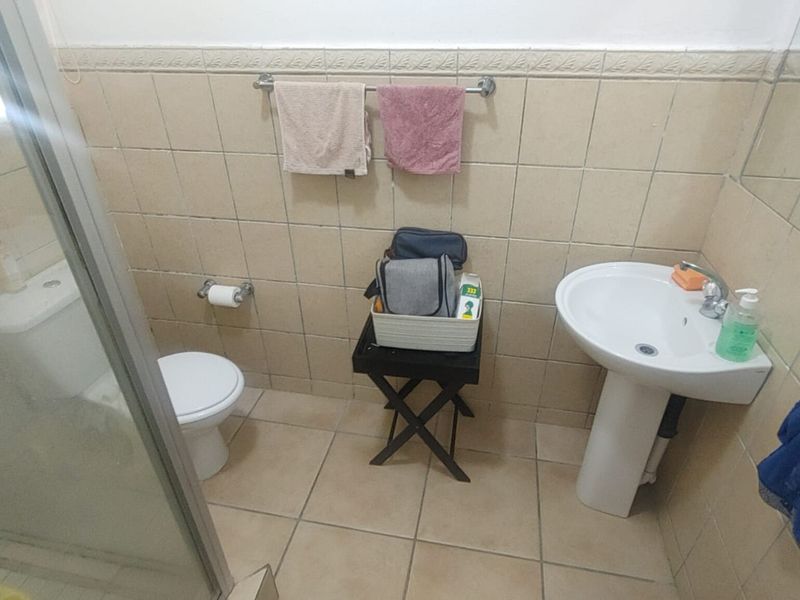 A functional bathroom featuring a pedestal washbasin, toilet, and a glass-enclosed shower with neutral ceramic wall and floor tiling.