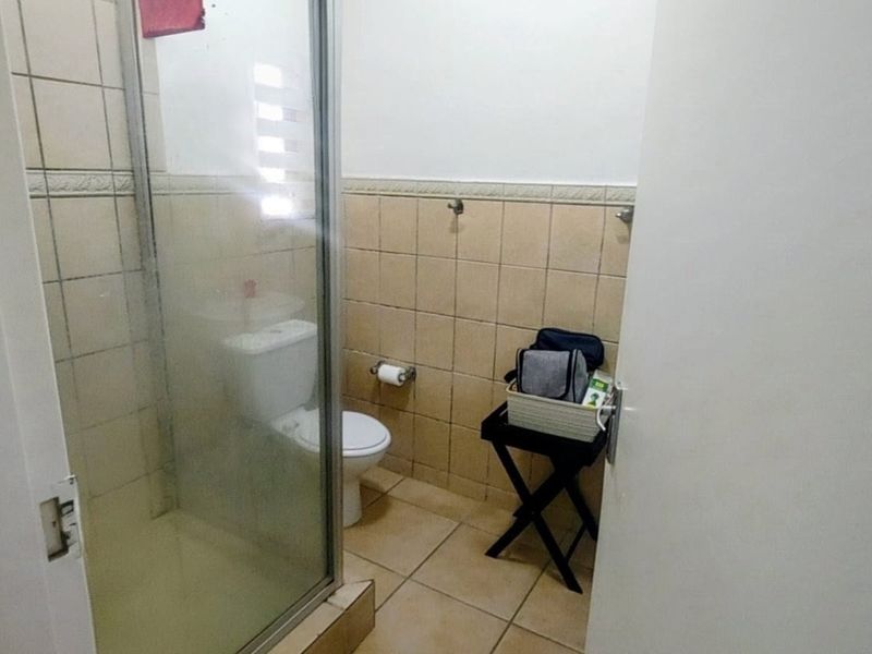 A compact bathroom featuring a glass-enclosed shower and a standard toilet with neutral ceramic wall and floor tiling.
