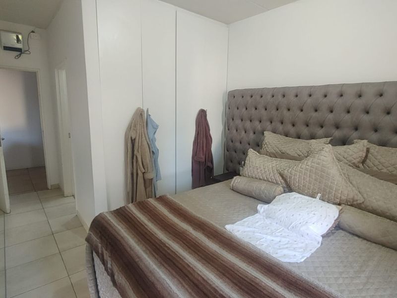 A bedroom featuring built-in cupboards and tiled flooring, providing a functional living space with direct access to an adjacent hallway.