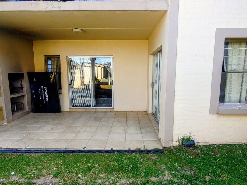 Covered patio area featuring tiled flooring, a built-in braai, and sliding glass doors with security gates, providing direct access to the apartment.