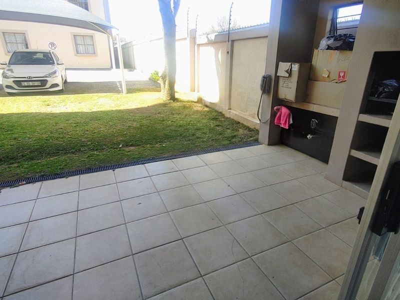 Covered patio area featuring tiled flooring and a built-in braai, overlooking a small private garden space.