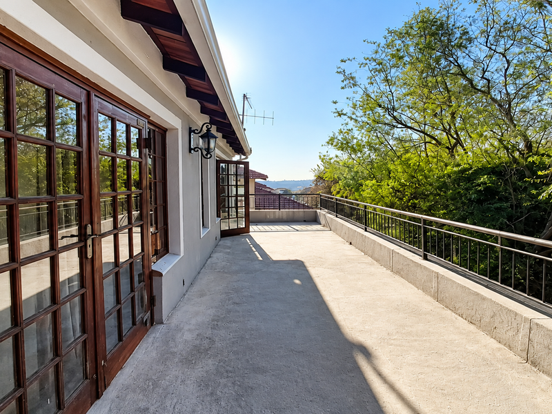 Spacious balcony featuring concrete flooring, timber-framed glass doors, and a metal balustrade, offering an open outdoor area with elevated views.