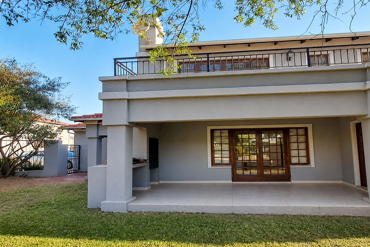 Rear view of the house featuring a spacious covered patio with a built-in braai and an upper-level balcony with metal railings.