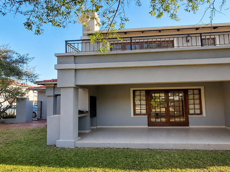 Rear view of the house featuring a spacious covered patio with a built-in braai and an upper-level balcony with metal railings.