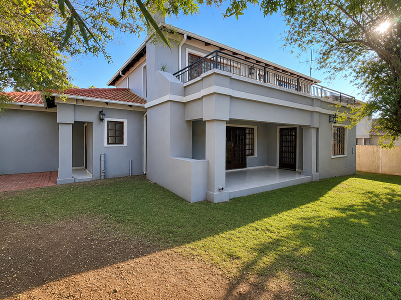 Rear view of the house featuring a covered patio, a balcony with metal railings, tiled roofing, and a well-maintained garden area.