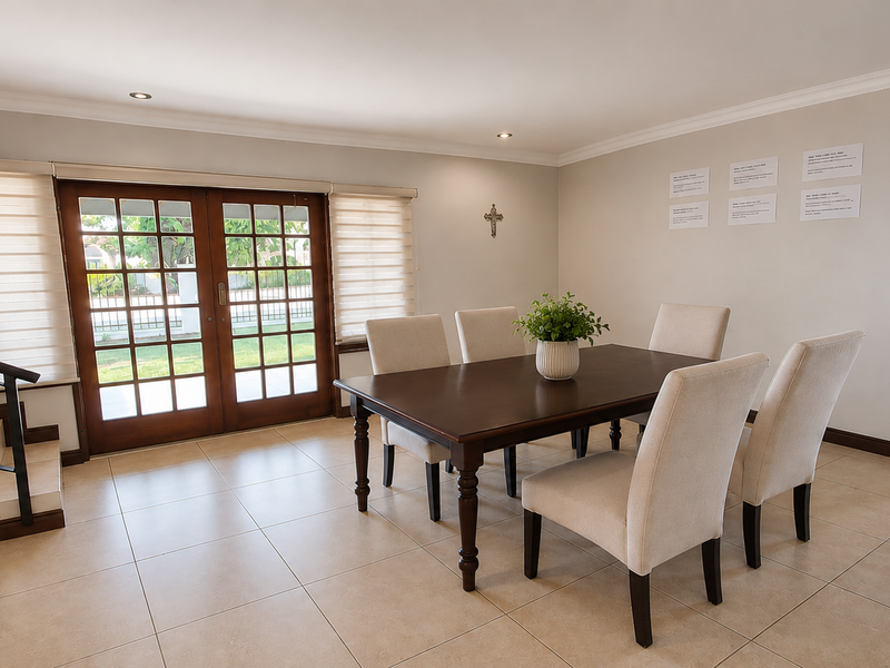 A bright dining room featuring tiled flooring, recessed lighting, and wooden french doors leading to the exterior, complemented by a staircase with metal railings.