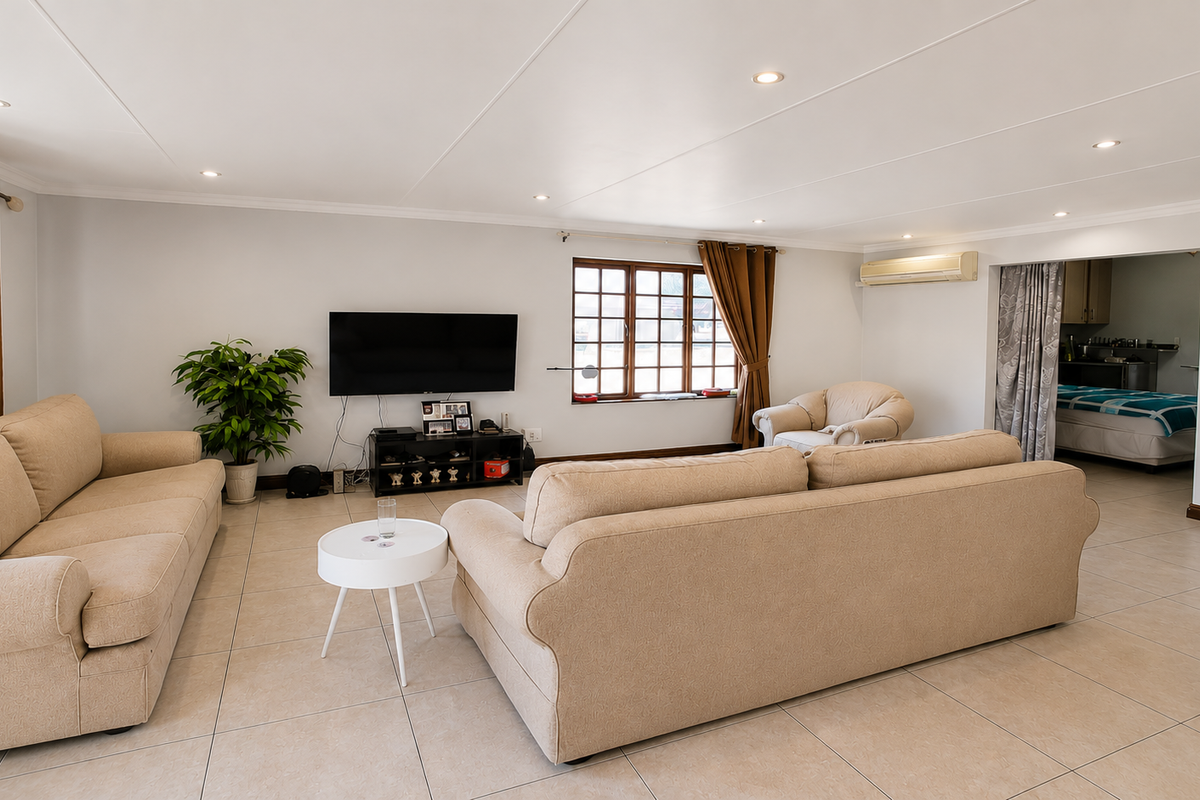 Spacious living room featuring neutral tiled flooring, recessed downlighting, and a wall-mounted air conditioning unit, with an open transition to an adjacent room.